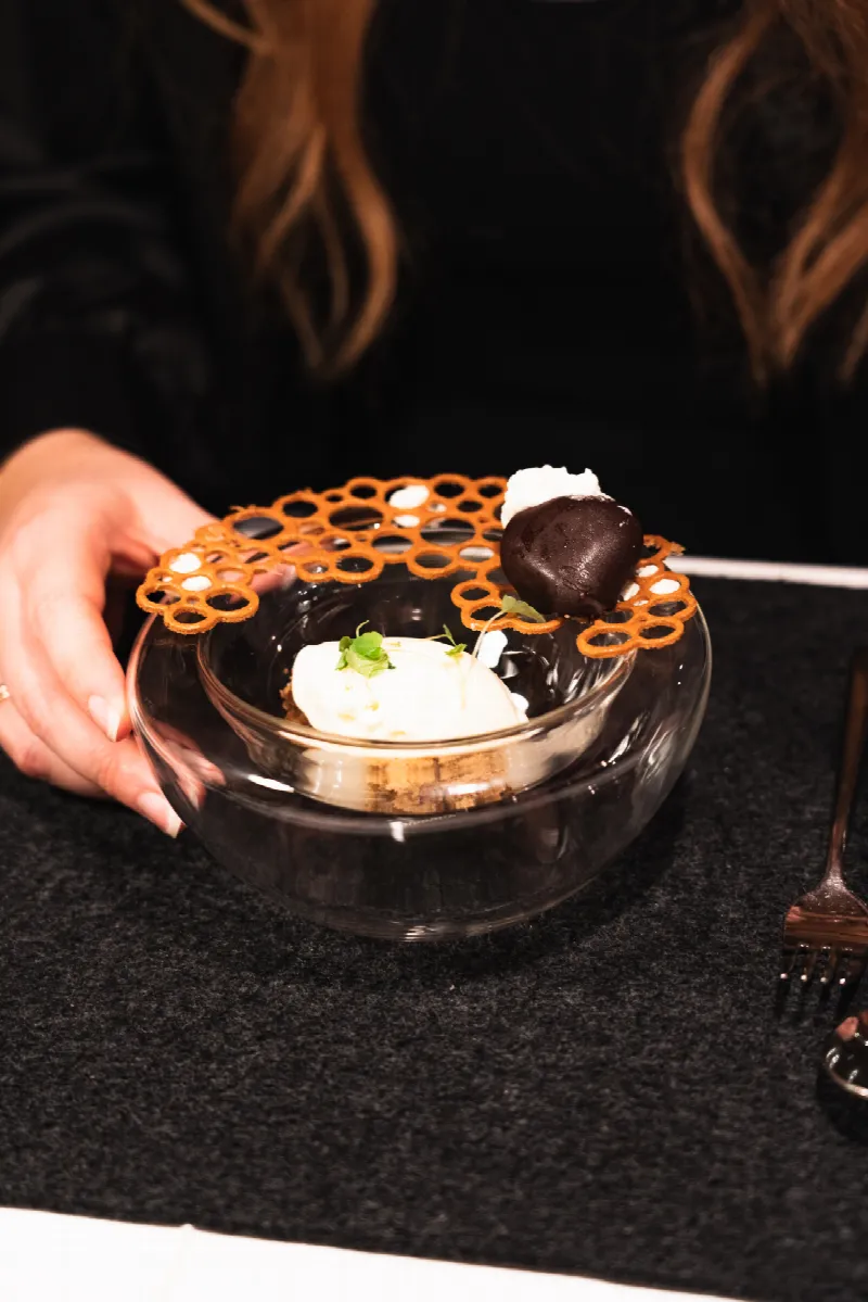 Dessert im Glas mit Creme, knusprigem Karamellgitter und Schokoladenpraline, serviert am Tisch